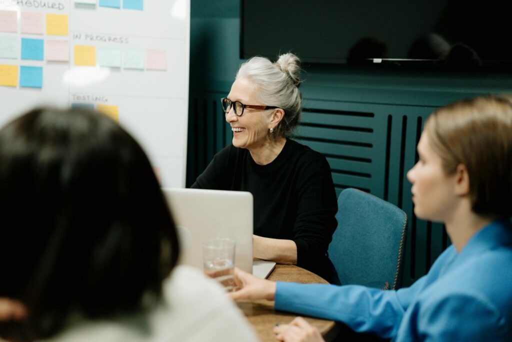 Lächelnde ältere Frau im Teammeeting vor einem Laptop, diskutiert über die Digitalisierung von Fotos und Dokumenten zur Effizienzsteigerung in Unternehmen.