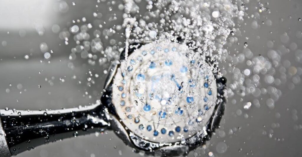  Nahaufnahme einer Duscharmatur, aus der Wasser strömt, mit deutlich sichtbaren Wassertropfen, die den Duschkopf umgeben. Das Bild zeigt die Präzision und Effizienz einer hochwertigen Duscharmatur im Einsatz.