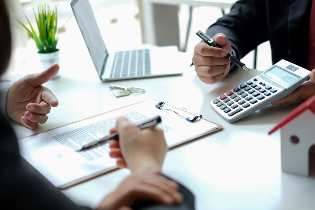 Zwei Personen sitzen an einem Schreibtisch mit Laptop, Taschenrechner und Dokumenten, während sie über finanzielle Strategien diskutieren. Das Bild symbolisiert professionelle Finanzberatung und Planung zur Erreichung finanzieller Unabhängigkeit