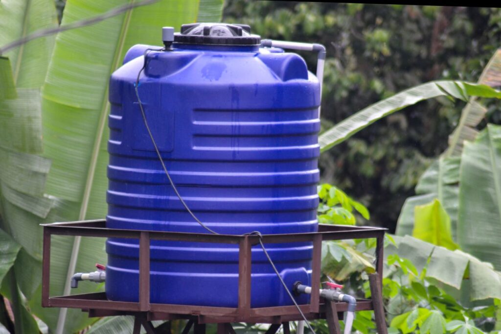 Grosse blaue zisterne auf Holzgestell im gruenn umgebenen Garten zur Regenwassernutzung und Wasserspeicherung im Aussenbereich