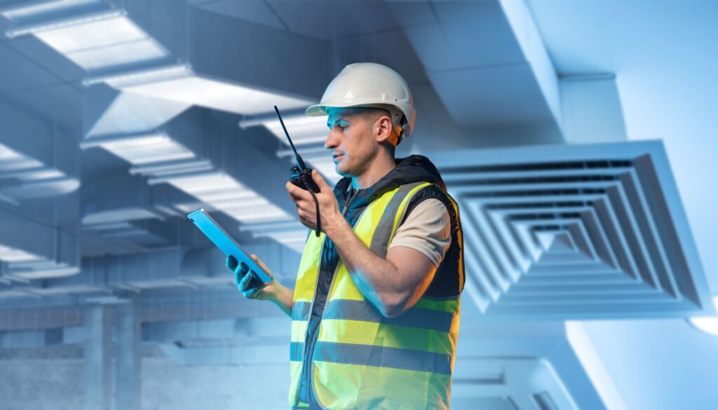 Ingenieur mit Tablet und Funkgerät überprüft Lüftungsanlage in einem Gebäude