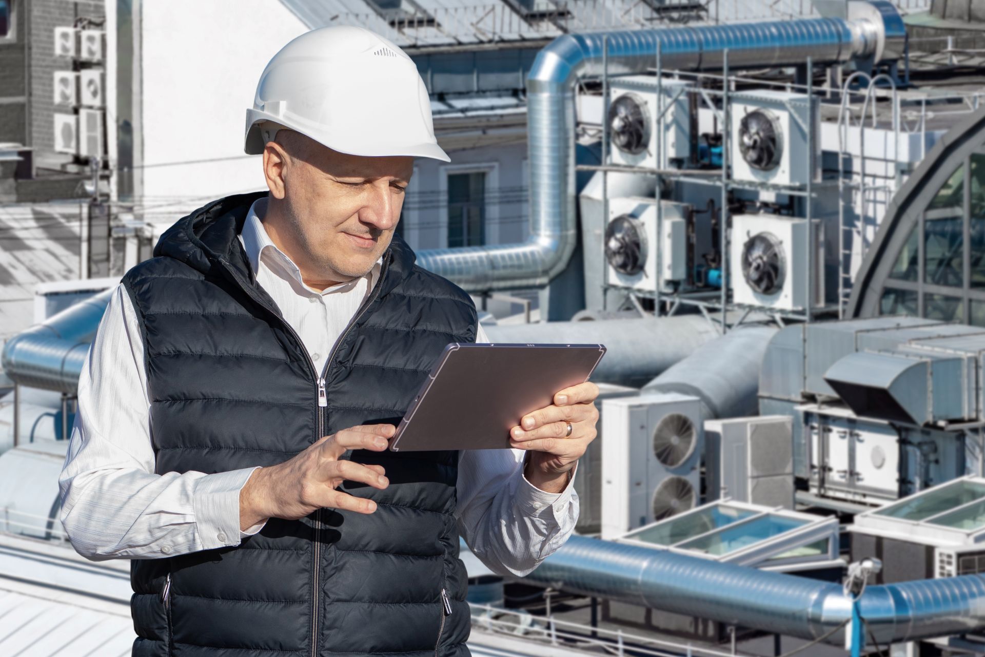 Ingenieur mit Tablet überprüft Lüftungs- und Klimaanlage auf Gebäudedach