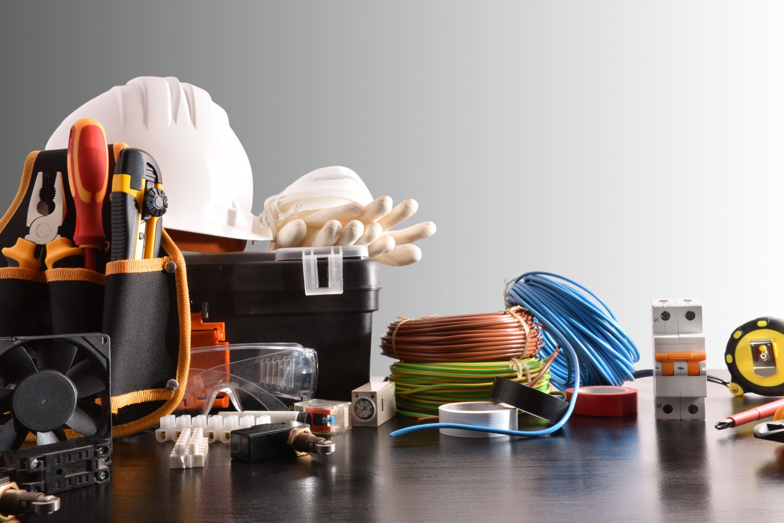 Ein Kabelbaum wird mit professionellen Werkzeugen, Schutzhelm, Isolierband und Kabelrollen vorbereitet
